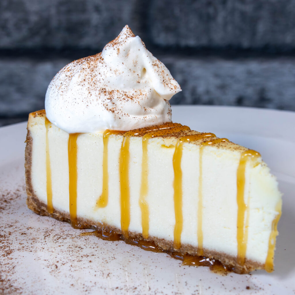 Slice of pumpkin cheesecake with graham cracker crust and whipped cream topping