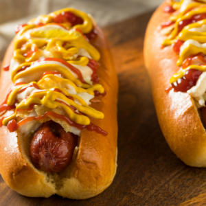 Two Hot Dogs with ketchup, mustard and onions on wood plate