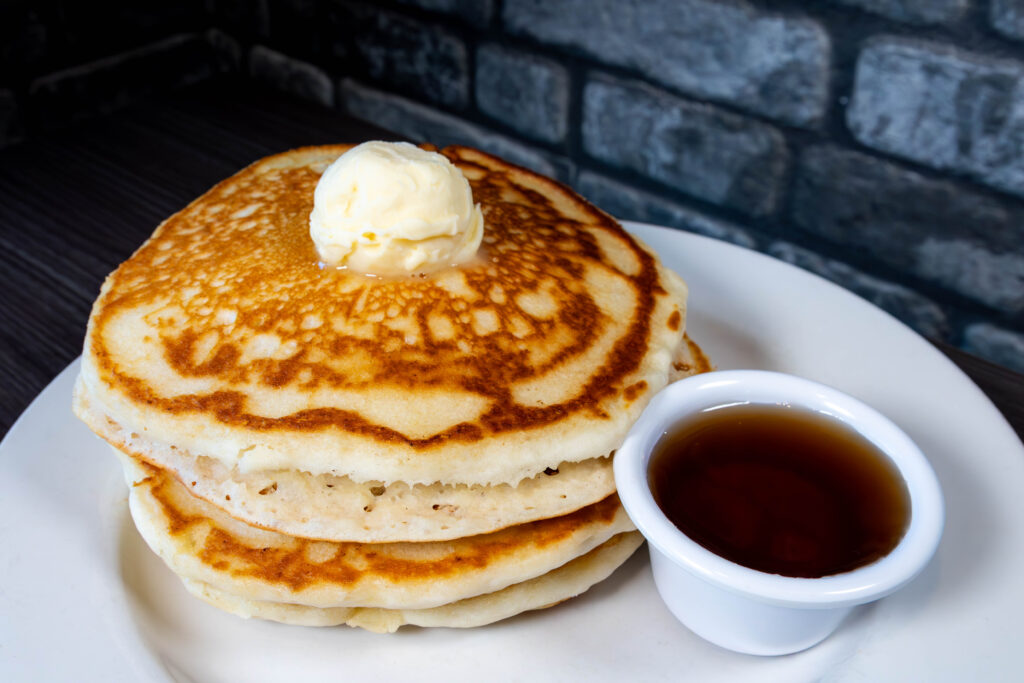 Stack of pancakes with butter on top and side of maple syrup